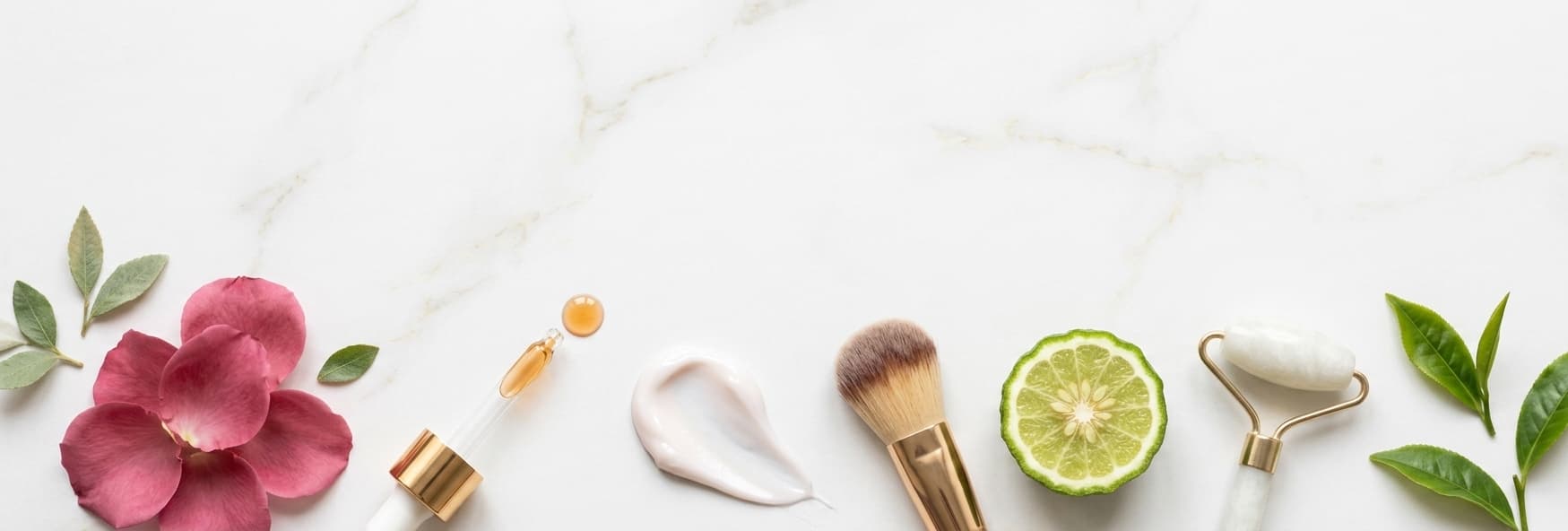 Skincare serums, brushes and botanicals laid out on marble